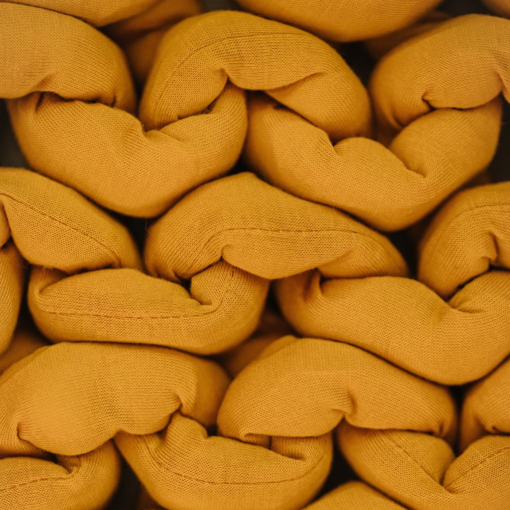 Close-up of thick, mustard-yellow strands woven in a chunky braid highlights the texture and stitching details of the Knit Weighted Blanket.