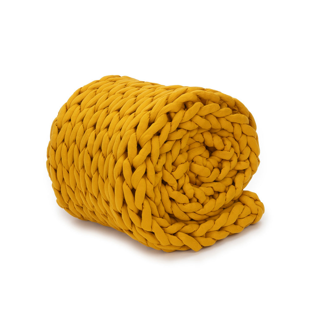 The Knit Weighted Blanket, in a bright mustard yellow, features thick chunky braids and is shown rolled up neatly against a plain white background.