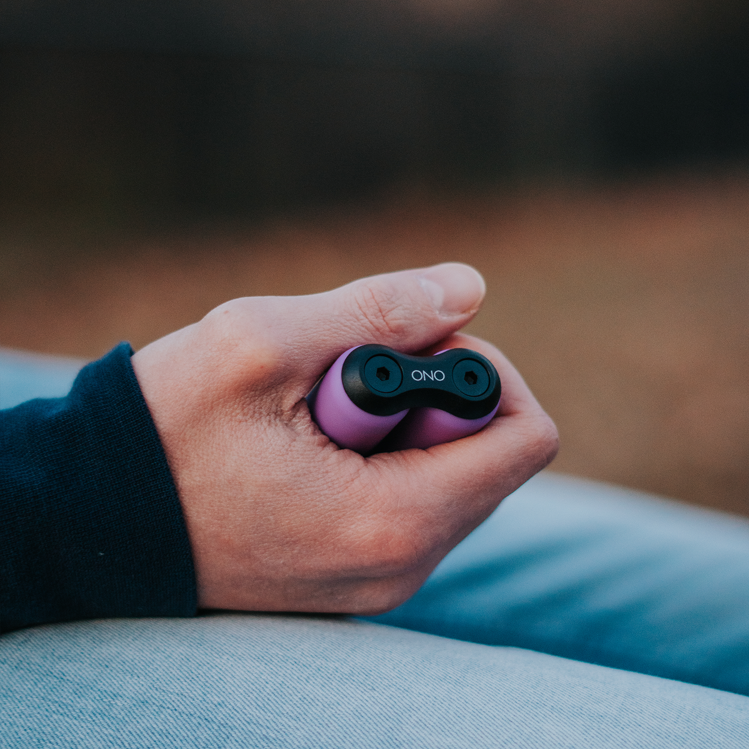 A hand holds a small, purple and black ONO Roller Soft Touch Plastic fidget toy with the thumb on top—ideal for stress relief—against a softly blurred background.