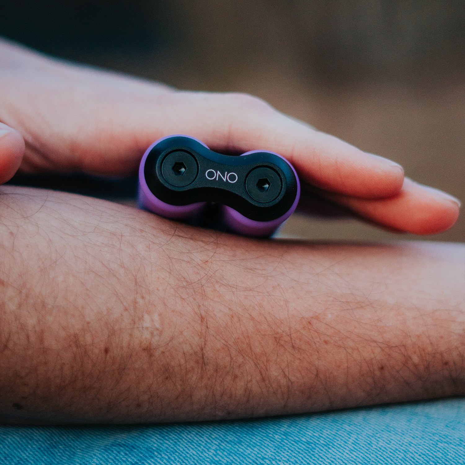 A close-up of a hand holding the ONO Roller Soft Touch Plastic, a small purple silent fidget toy, against their forearm with a blurred background.