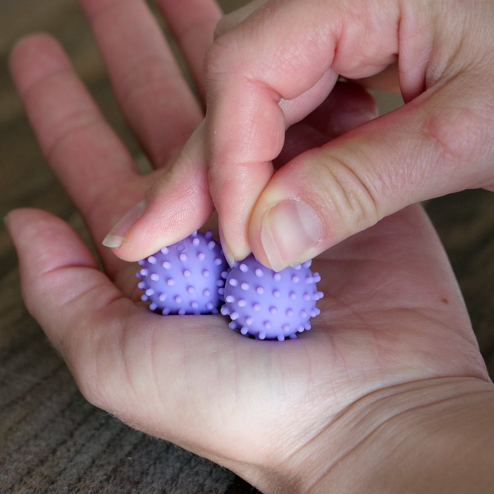 A hand holds two small purple ONO Sigbits, while another pinches one between the thumb and index finger, providing sensory stimulation and serving as a calming fidget toy.