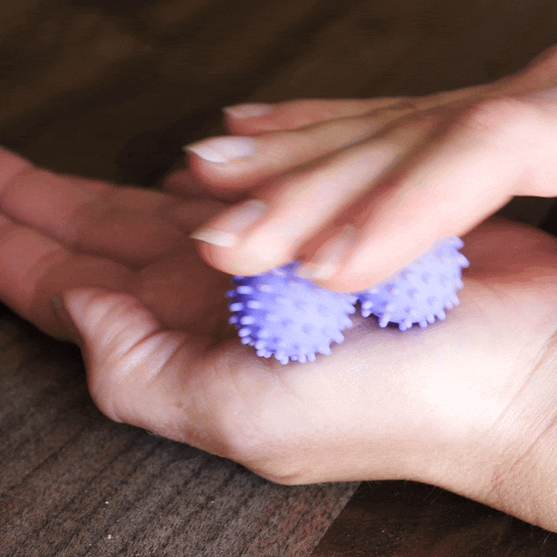 A person rolls two ONO Sigbits—small, spiky purple fidget toys—between their hands on a wooden surface for sensory stimulation.