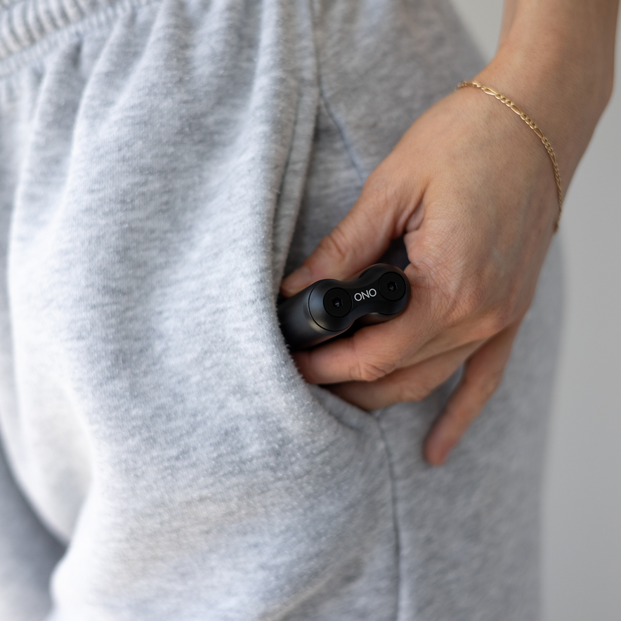 A person in light gray sweatpants tucks a small black ONO Roller Aluminum into their pocket, their hand partially visible as they fidget with a gold bracelet on their wrist.