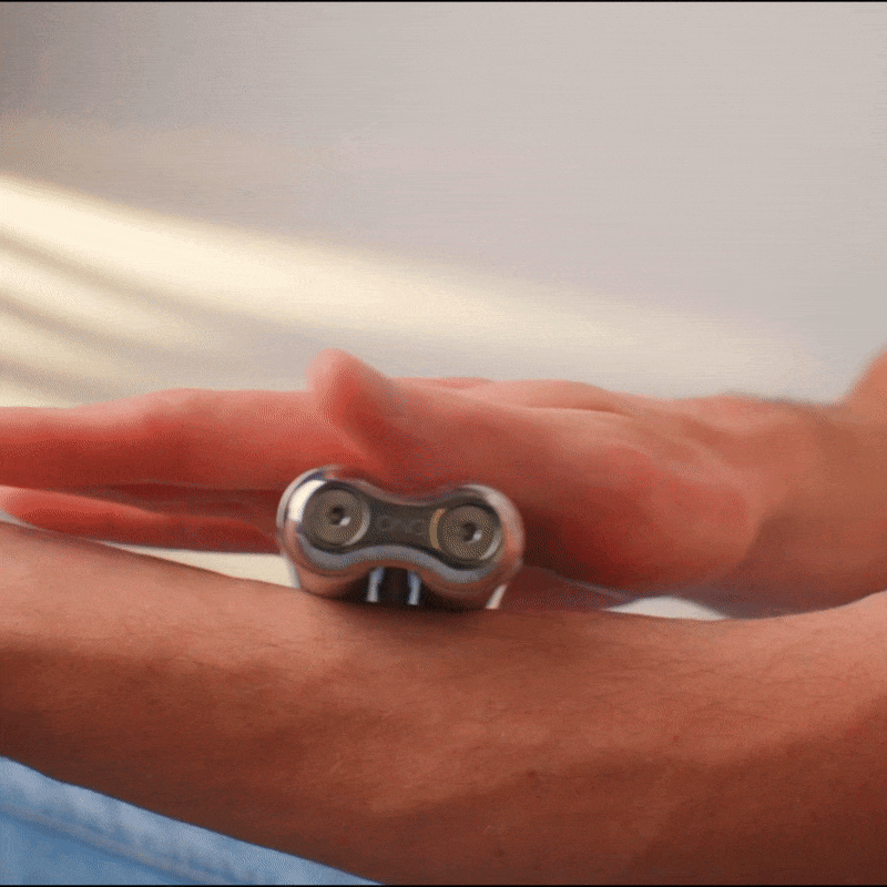 Using their other hand, a person rolls the ONO Roller Steel—a small massage tool with dual rotating balls—along their forearm.