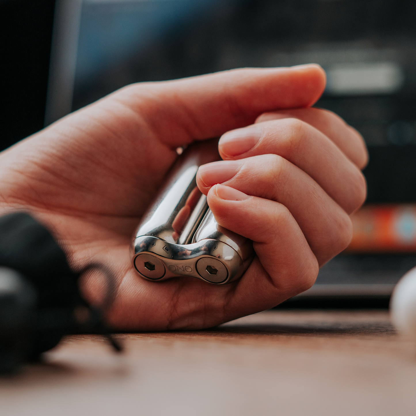 A close-up shows a hand holding two polished ONO Roller Steel cylinders, with a blurry laptop keyboard and screen in the background.