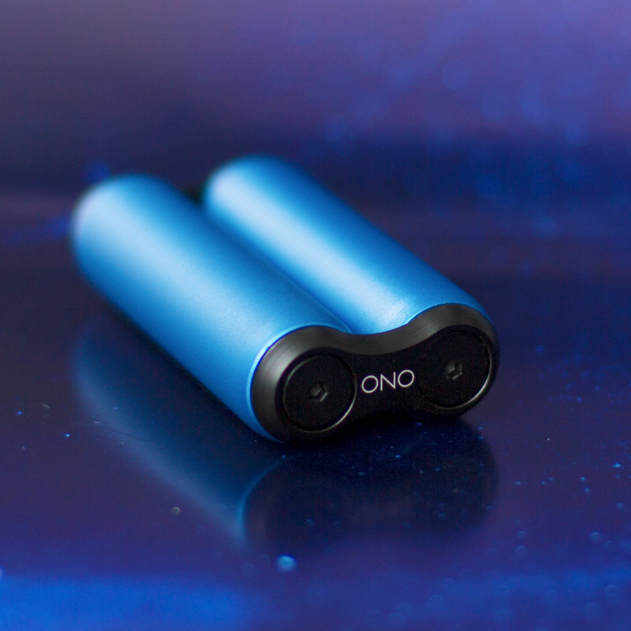Two blue ONO Roller Aluminum fidget toys with black ONO-marked ends sit side by side on a glossy purple surface. Their circular indented ends invite fidgeting, while blurred blue and purple hues color the background.