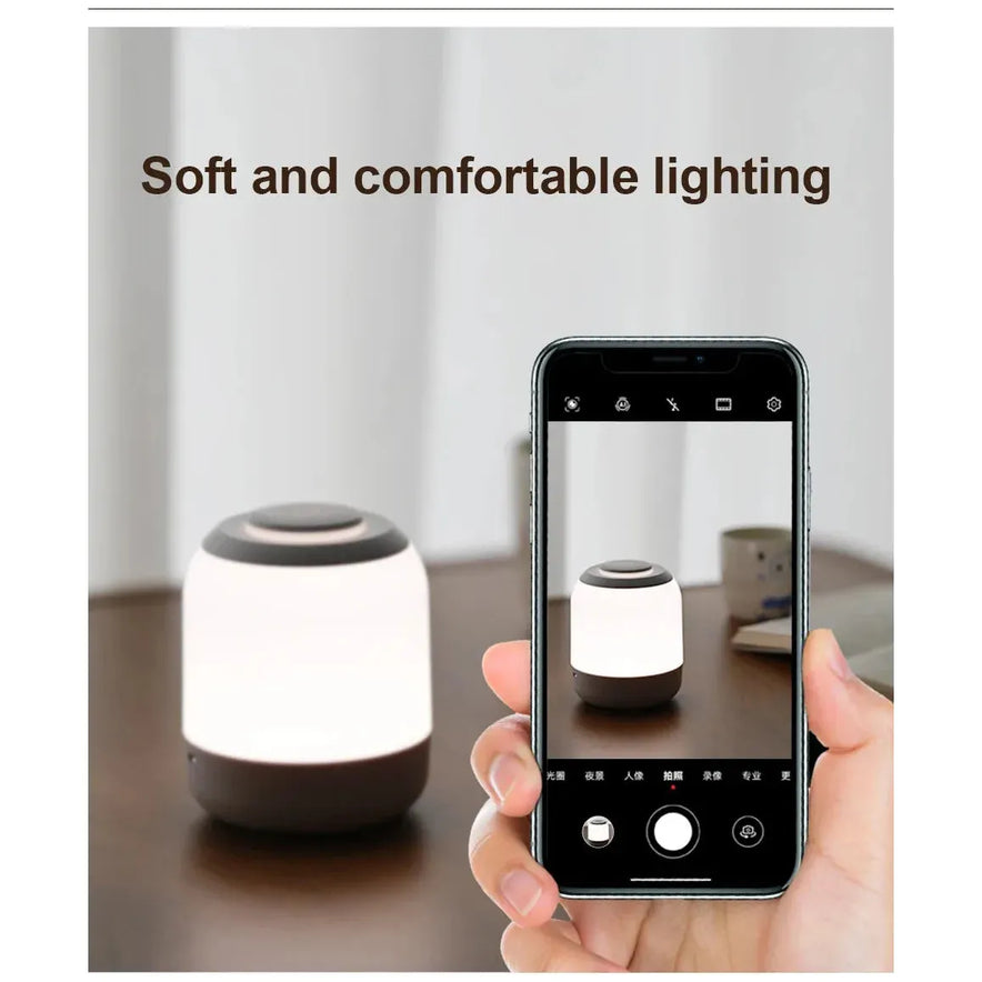 A smartphone captures a photo of a softly lit Touch Control LED Night Light Lamp, which is USB rechargeable and emits a warm glow. The cylindrical lamp features 3 color settings and text in the background reads, Soft and comfortable lighting.