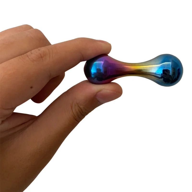 A hand holds the Stainless Steel Knucklebone Fidget Tool for Anxiety Relief and Focus Enhancement, a small metallic toy with an iridescent dumbbell shape in blue, purple, and yellow.