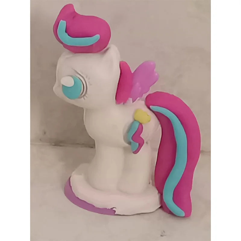 A handmade clay model pony with bright pink hair, wings, a white body, blue eyes, and blue/yellow mane accents resembles the playful My Little Pony Play-Doh creations from TAKARA TOMY. It stands proudly on a small circular base.