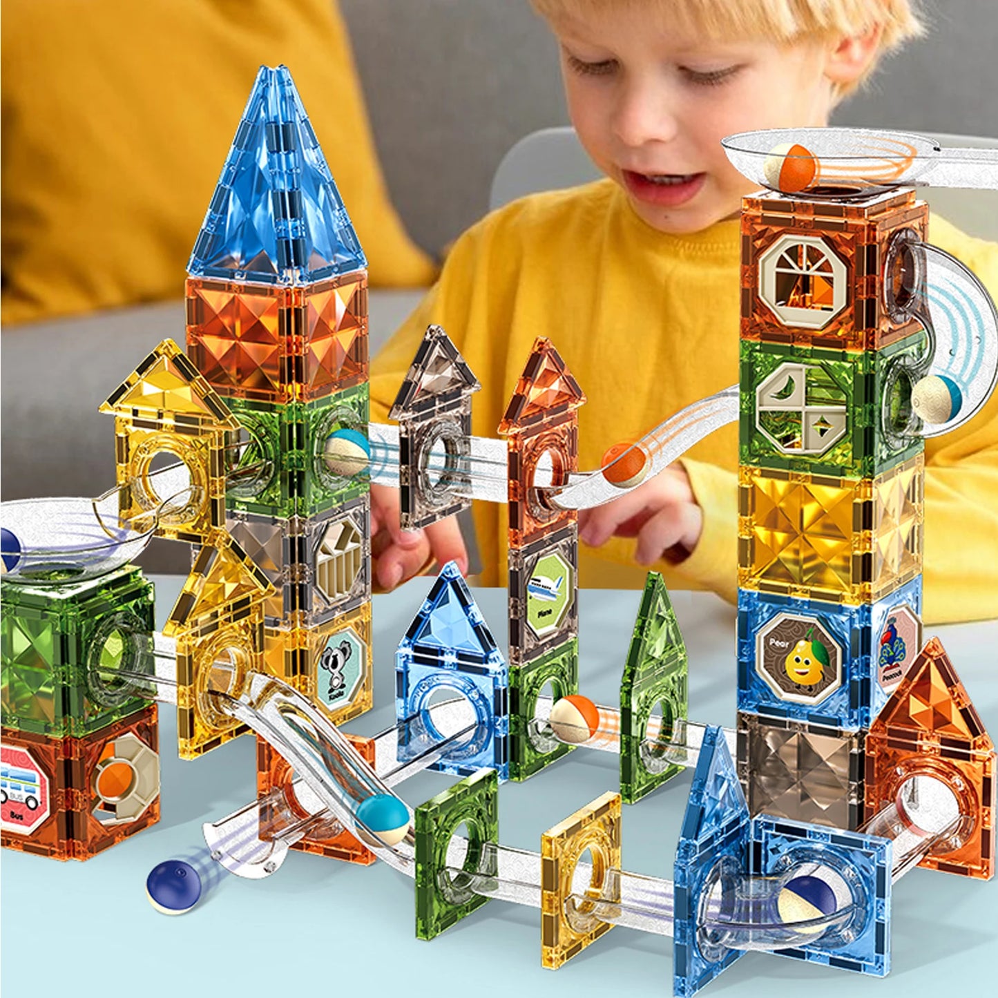 A child engages in STEM learning with the Magnetic Marble Run Building Blocks Set, featuring transparent marble tubes and colorful towers made from red, blue, green, and yellow pieces.