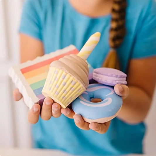 A person in a blue shirt holds colorful, squishy toy desserts like a rainbow cake slice and blue donut—playful creations reminiscent of the Melissa and Doug Sweet Shop Multicolored Chalk and Holders Play Set, 33 Pieces.