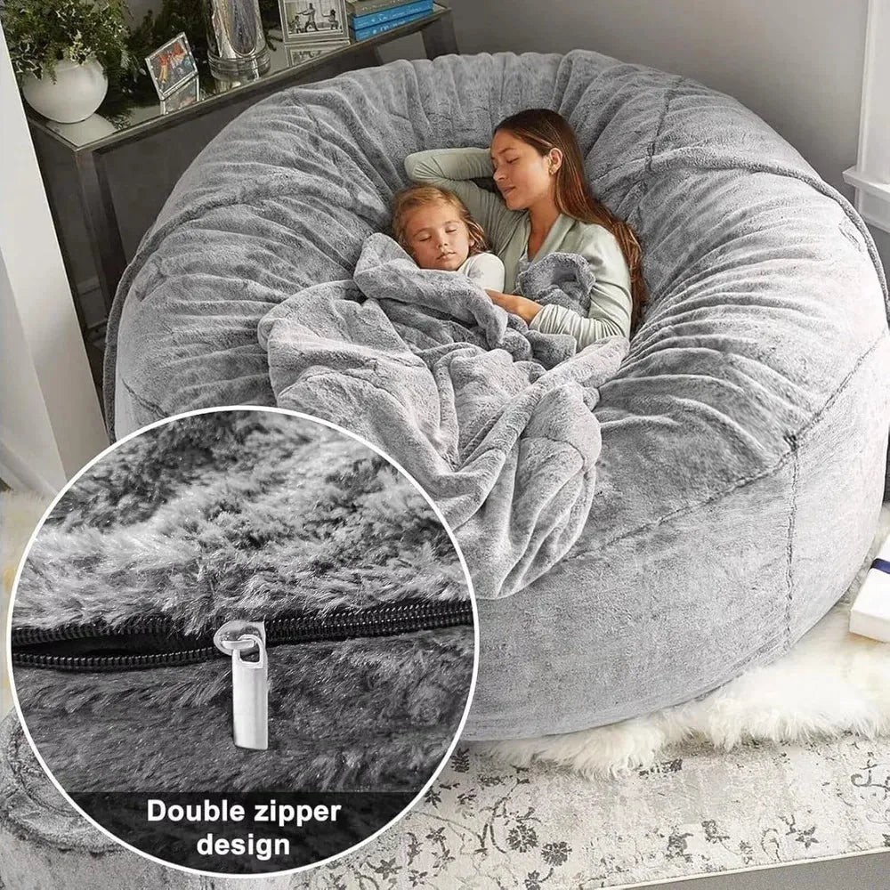 Two people are cozily snuggled under a blanket on the Giant 6FT Cozy Plush Bean Bag Chair for Adults and Families, featuring luxurious faux fur texture and a double zipper. The setting is indoors with a nearby plant.