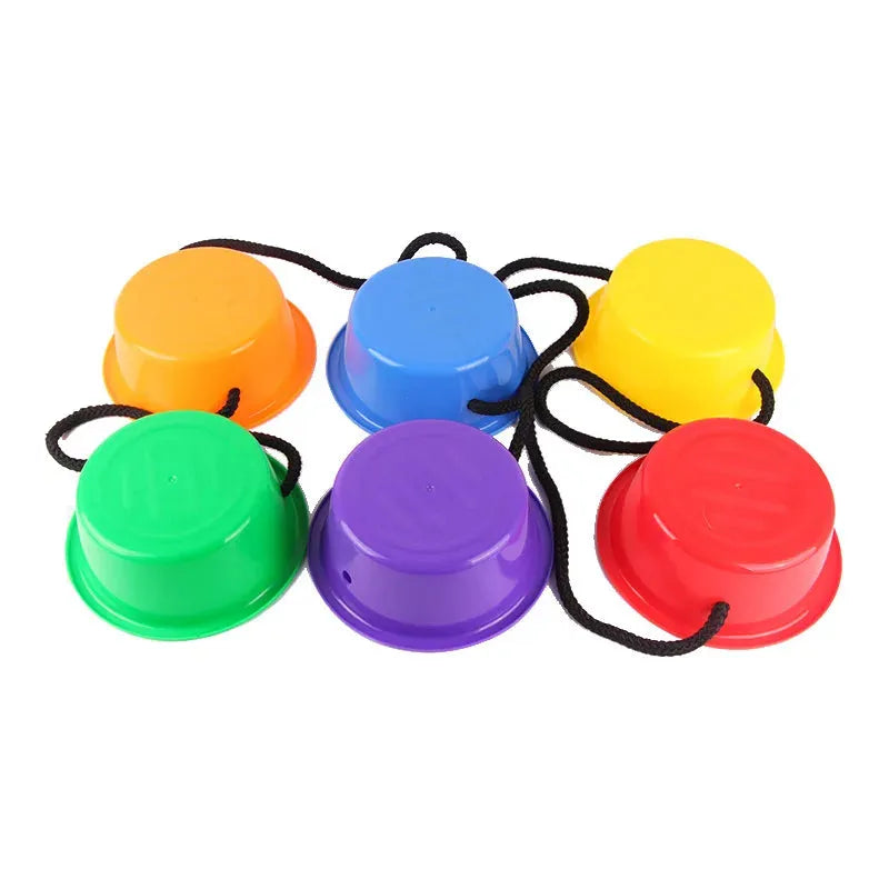 The Montessori Colorful Balance Stones, in orange, yellow, red, green, blue, and purple and linked by black ropes, form a circle of six inverted cups. They promote sensory integration and enhance developmental play through balancing activities.