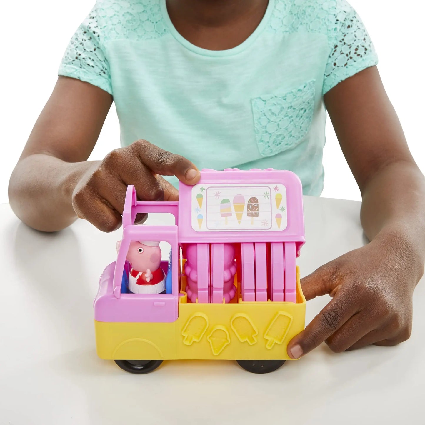A child in a teal shirt plays with the Play-Doh Peppas Ice Cream Playset, a colorful toy truck from the Peppa Pig collection, featuring a cartoon pig driver and playful ice cream decorations.