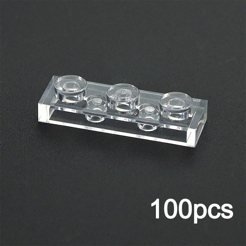 A transparent 1x3 brick from the MOC Transparent Bulk Brick Set, compatible with Lego, is displayed on a black surface. “100pcs” in white highlights this versatile clear building block collection for wall panels and house parts.