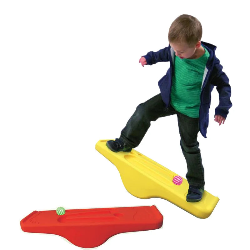 A child in a blue jacket and green shirt balances on a yellow Interactive Outdoor Balance Board Seesaw for Kids, while an orange one with a colorful ball rests nearby. Perfect for sensory training!.