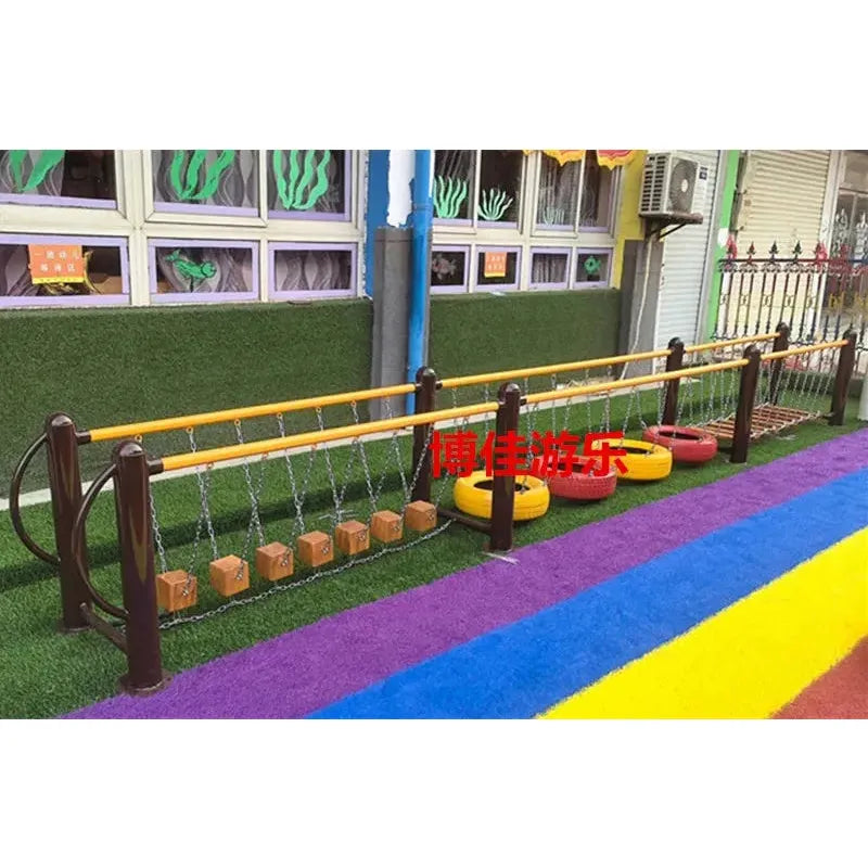 A vibrant unisex playground with balance beams of wooden blocks, suspended tires, and a net section. Perfect for ages 3-8, the ground showcases bright green, purple, blue, and yellow stripes. A nearby building has windows and sea-themed decor. Featured item: outdoor toys; Childrens swings; Climbing nets; Swinging bridges; Drilling Sensory integration Equipment.