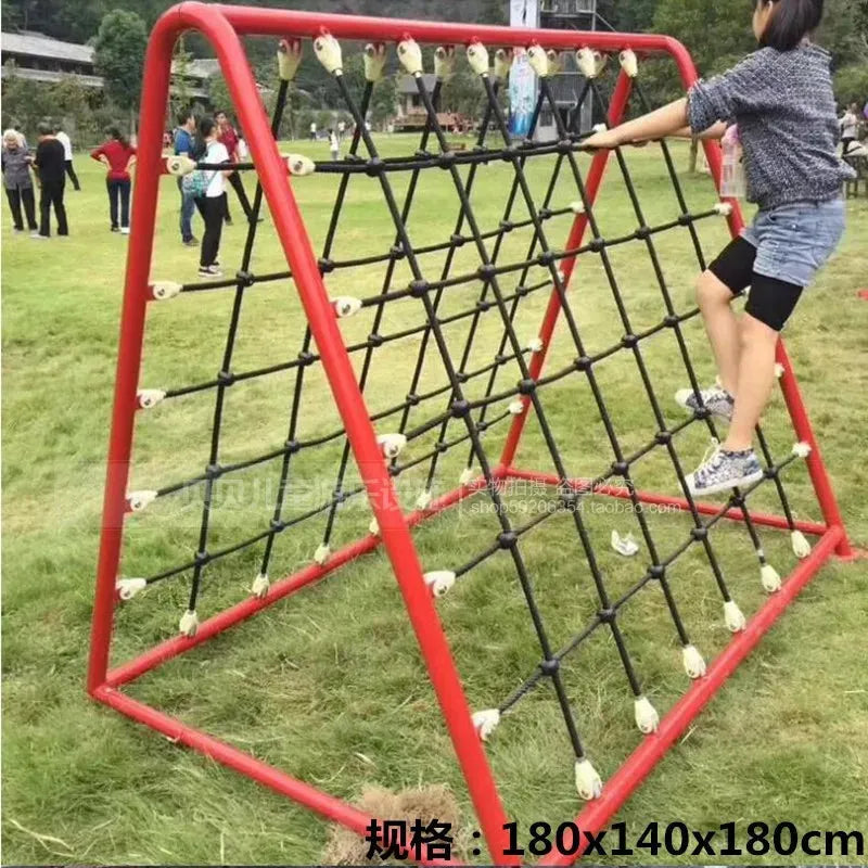A child climbs the Outdoor Steel Climbing Frame Swing, a bright red metal structure perfect for sensory integration training on a grassy field. In the background, others enjoy the day amid distant trees and buildings, enhancing engaging activities for children.