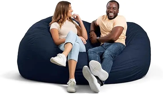 Two people sit comfortably on the Fuf XXL Foam Filled Bean Bag Chair in Cobalt, 6 Feet. Both are smiling, casually dressed in light shirts and jeans, looking relaxed and engaged with each other.