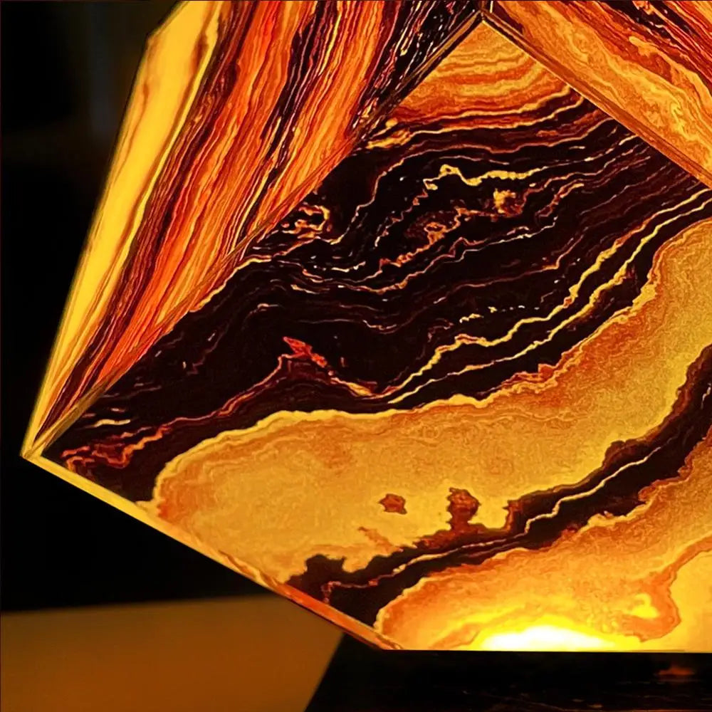 The Elegant Agate Crystal Table Lamp features a geometric design with swirling orange, black, and brown patterns similar to wood grain or marble. This artistic piece emits a warm glow, perfect as bedroom or living room décor.