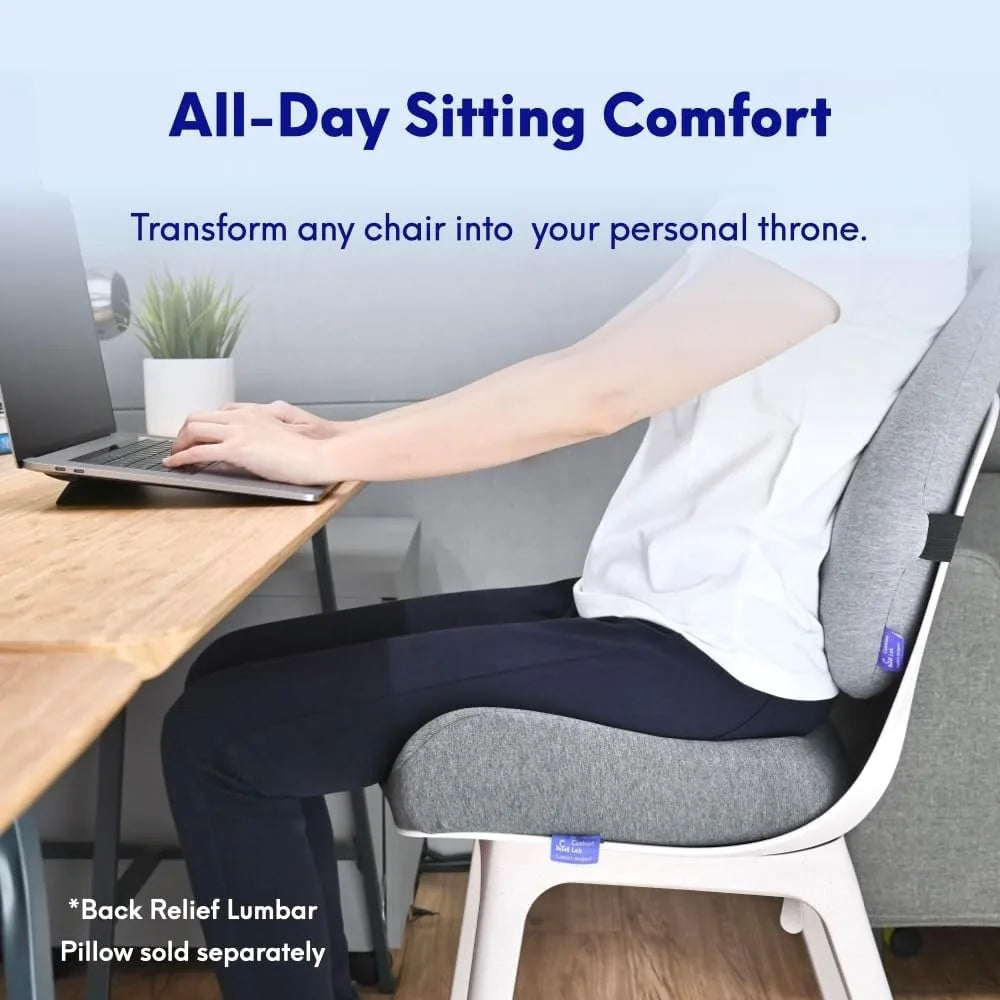 A person sits comfortably on a white chair using the Cushion Lab Patented Pressure Relief Seat Cushion while working on a laptop at a desk. The text reads: All-Day Sitting Comfort. Transform any chair into your personal throne. Note: Back relief lumbar pillow sold separately.