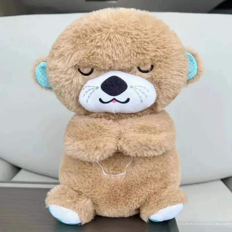 A Soothing Otter Musical Plush Toy sits on a surface with closed eyes and a peaceful expression. Featuring dark gray fur, its designed as a sensory sleep companion for newborns, providing light and sound comfort against a light-colored background.