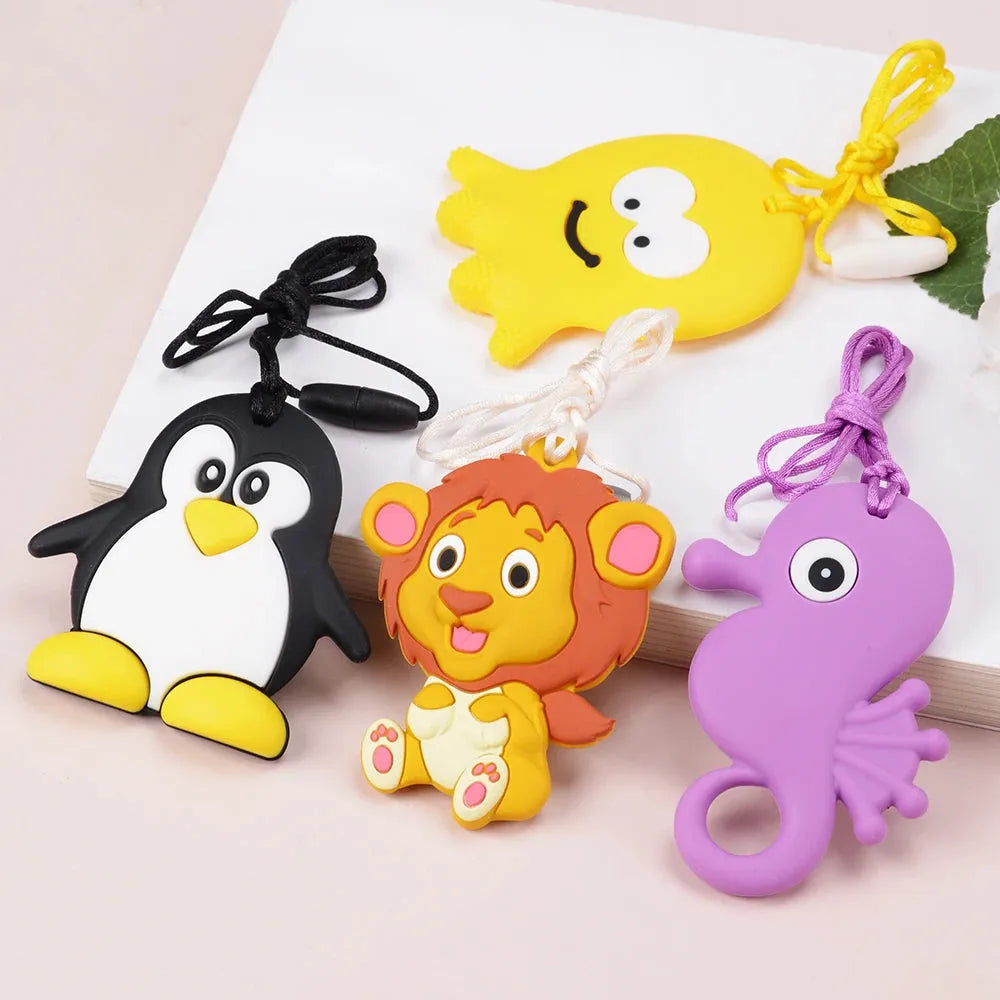 Four vibrant silicone chewable necklaces for kids, designed as oral motor therapy tools, feature a yellow octopus, a black and white penguin, a brown lion, and a purple seahorse. Each pendant comes with a matching string on display against a light surface.
