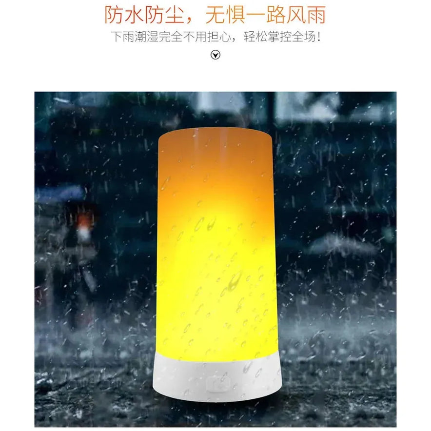 The Simulated Flame LED Night Light, shaped like a cylinder, glows yellow in the rain. Raindrops enhance its realistic flame effect, while elegant Chinese text above hints at its versatile use in different settings.