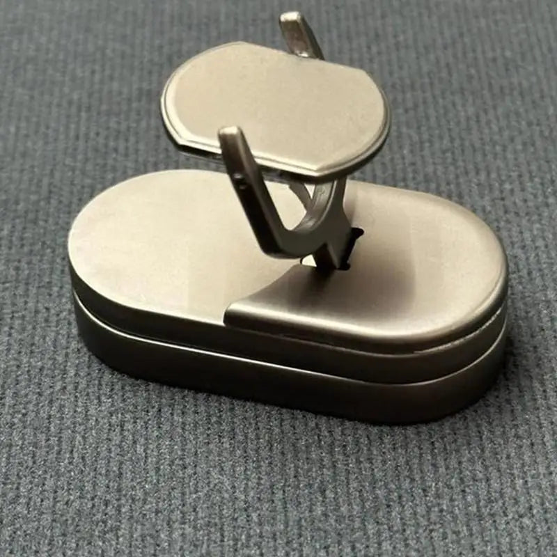 The Fidget Slider Magnetic Metal Spinner Toy, featuring a metallic rounded rectangular base and rubber accents, with a raised rectangular piece held by two supports, is shown on a gray textured surface.