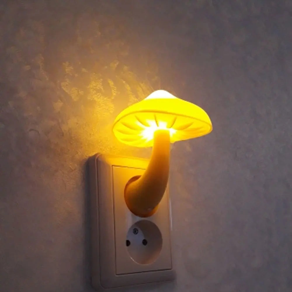 The Mushroom LED Night Light with Sensor Control, offering a warm white glow, plugs into a wall socket. Its mushroom shape softly illuminates against a textured wall, featuring automatic brightness adjustment for perfect ambiance.