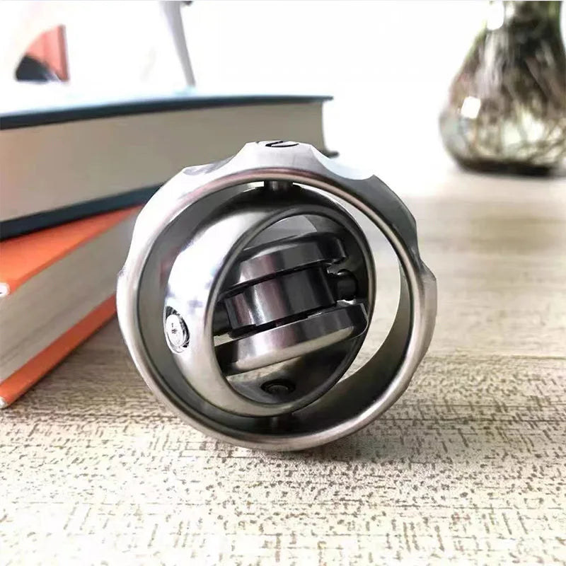 The Stainless Steel Fidget EDC Gyroscope Spinner, a sleek stress relief toy for adults and a unique gift, features an intricate spherical design on a wooden surface, with books and a blurred vase in the background for a serene setting.