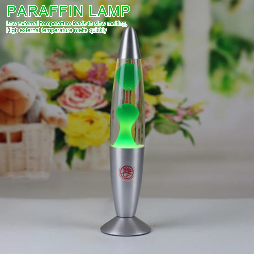 The Luminous Volcano Lava Jellyfish LED Night Light, with a silver base and top, stands on a white surface creating a relaxing ambiance. The blurred background has flowers. Text reads: 25W Atmosphere Lamp: Low temperature slows melting; high temperature quickens it.