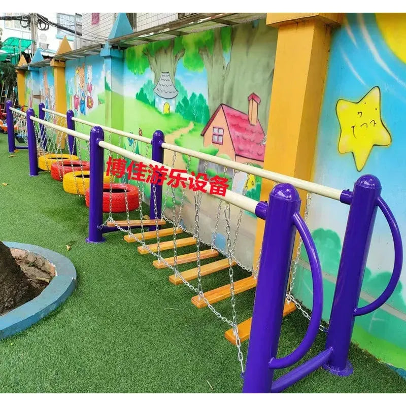 The playground features a colorful swinging bridge with chains and steps, perfect for ages 3-8. Unisex appeal is enhanced by a vibrant mural of trees and houses, an artificial grass ground, and complemented by metal toys from the outdoor toys lineup including swings and climbing nets.
