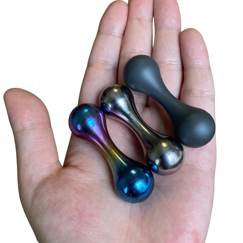 A hand holds three Stainless Steel Knucklebone Fidget Tools, resembling dumbbells with smooth, reflective surfaces in metallic blue, silver, and dark grey. The polished finish enhances finger dexterity and provides soothing anxiety relief.