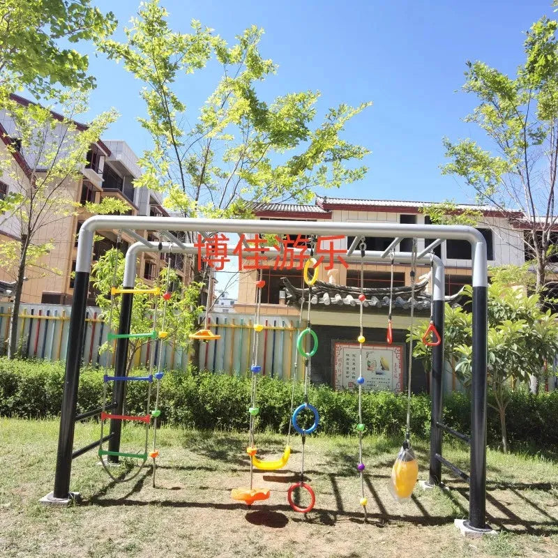 Under a bright blue sky, unisex outdoor toys like Childrens swings, Climbing nets, Swinging bridges, and Drilling elements enhance physical training and sensory integration. These vibrant items are surrounded by green grass, trees, buildings, and a fence in the background.