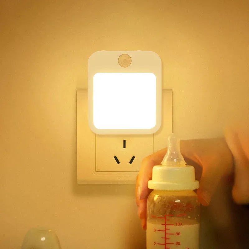 The Dimmable Motion Sensor LED Night Light with EU Plug creates a cozy, energy-efficient glow in any babys room, bedroom, or corridor. It offers a comforting ambiance as a hand holds a baby bottle near the warm light.