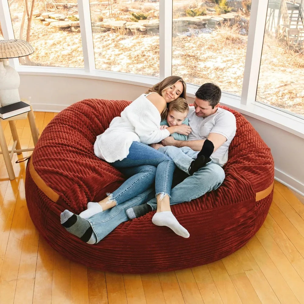 A family of three—two adults and a child—relax together on the Fuf XXL Foam Filled Bean Bag Chair Deep Terracotta 6 Feet, enjoying a sunlit room with curved windows and wooden floors.