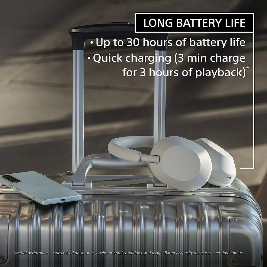 A pair of Sony WH-1000XM5 Wireless Noise Canceling Headphones with Integrated Processor V1 and 30-hour battery life rests on a silver suitcase. On-screen text highlights best-in-class noise cancelation and long battery life.