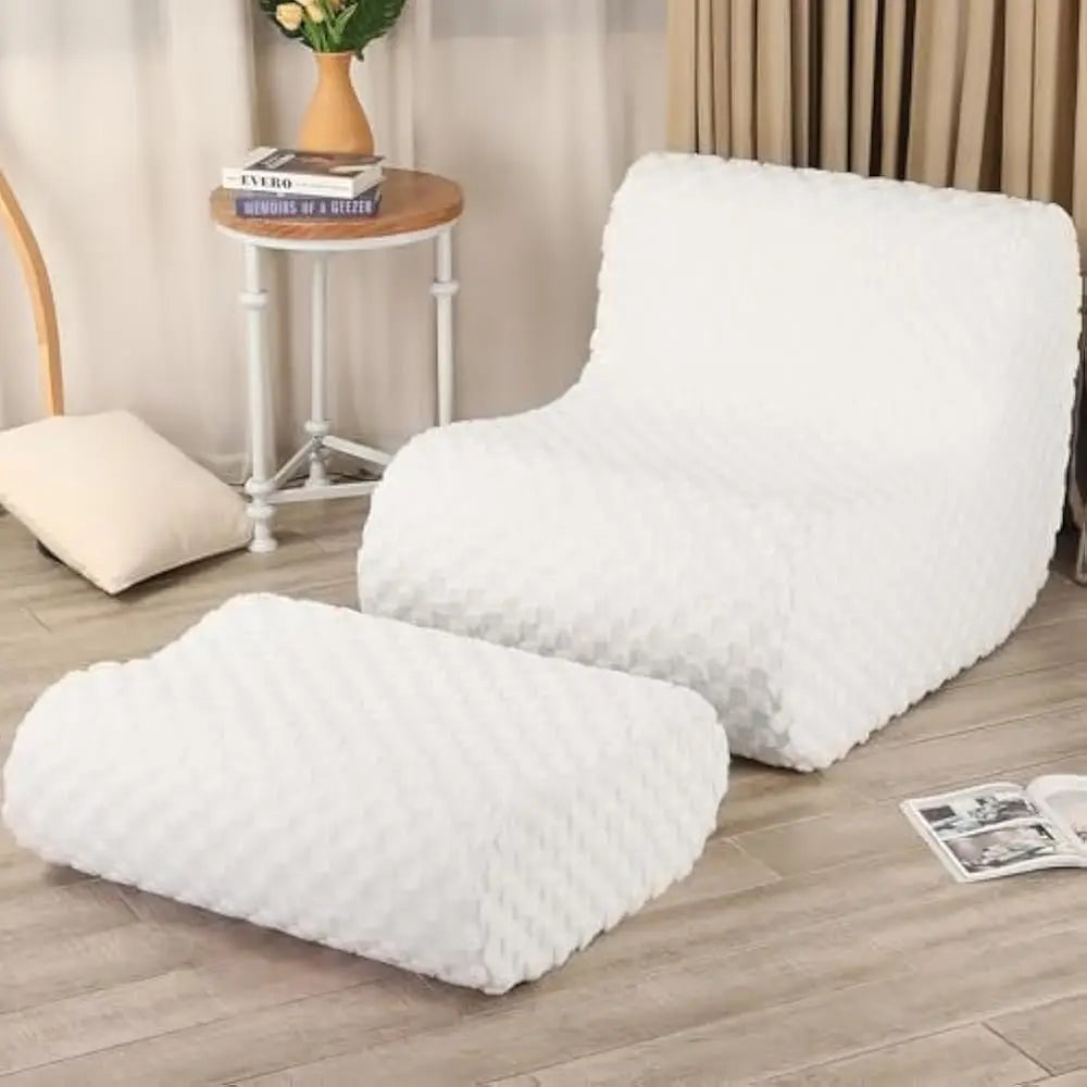 A modern Bean Bag Sofa in Standard-Cream with matching footstool sits on a light wooden floor by a round side table, pillow, and beige curtains, creating a cozy spot for reading or relaxing in the living room or bedroom.