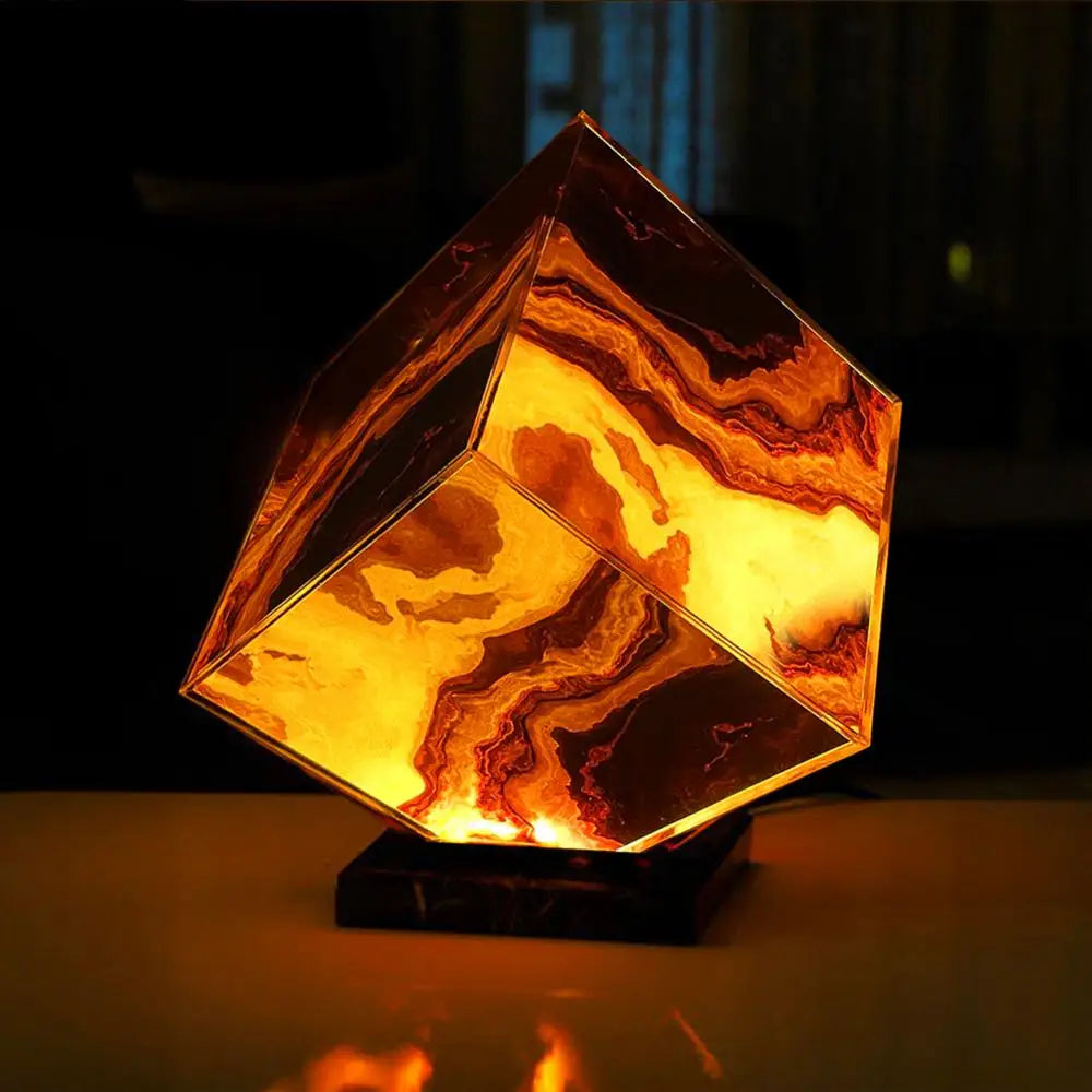 The Elegant Agate Crystal Table Lamp, with its cube shape and swirling amber and brown patterns on a dark base, resembles fiery abstract art, casting a warm glow. Perfect as bedside decor, it adds charm and elegance to your bedroom or living room.