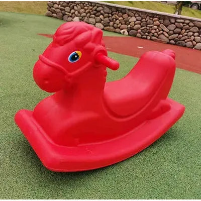 A vibrant childrens rocking horse on a green play surface outdoors, with a stone wall and grass in the background. This bright red horse features a blue eye and handles for gripping, making it an ideal toddler gift.