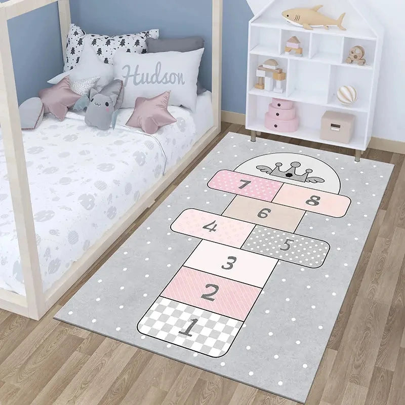 A children’s bedroom with a bed, stuffed toys, a personalized pillow, a white shelf with decor, and the Childrens Play Hopscotch Carpet in 03 color as a decorative anti-slip rug on the wooden floor.