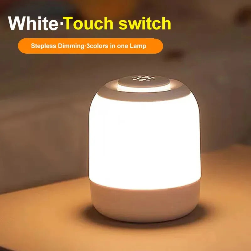 A touch-control LED night light lamp emits warm light with text reading White Touch switch and Stepless Dimming 3 colors in one Lamp. This USB rechargeable, cylindrical lamp is elegantly placed on a flat surface, ideal for kids and babies bedside or desk lighting.
