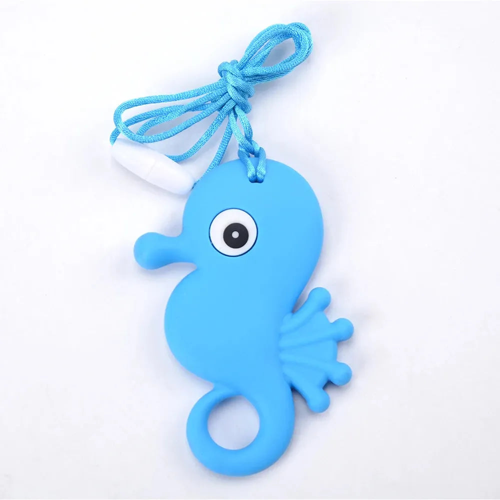 The Silicone Chewable Necklace for Kids, a sensory teether pendant shaped like a blue seahorse with a large eye and textured fin, is ideal for oral motor therapy. It hangs on a blue cord with a white clip, its playful design highlighted against the plain white background.