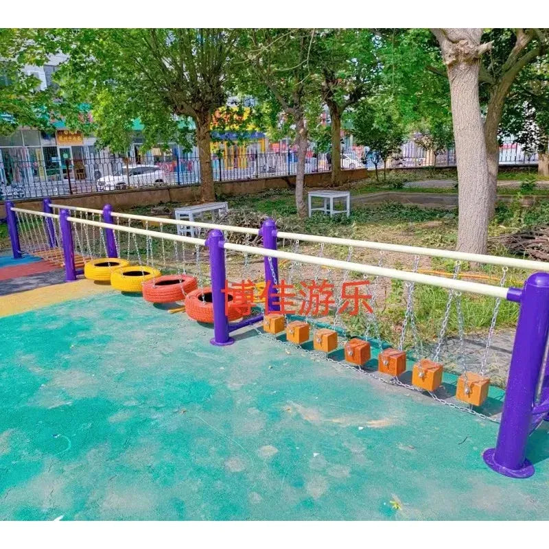The outdoor toys set includes colorful suspended tires and wooden blocks on ropes with purple and yellow rails, suitable for children aged 3-8. Featuring sensory integration for physical training, it has a green rubber floor surrounded by trees and fencing.