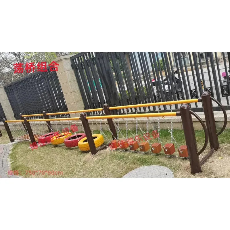 The outdoor toys set includes childrens swings, climbing nets, swinging bridges, drilling features for sensory integration, and physical training. Its designed for ages 3-8 on grassy terrain and enclosed by a black fence and stone wall.