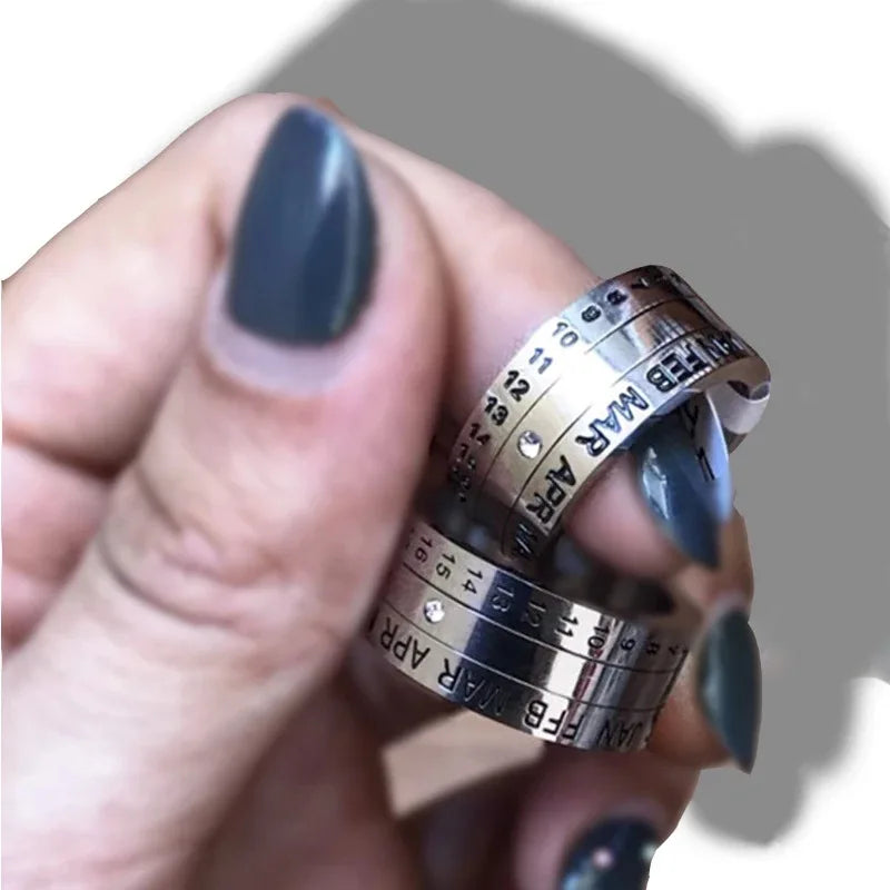 A hand with dark-painted nails holds two Stainless Steel Anxiety Rings for men and women—rotating calendar date fidget spinner rings. The overlapping silver bands offer a modern, timeless alternative to classic engagement rings.