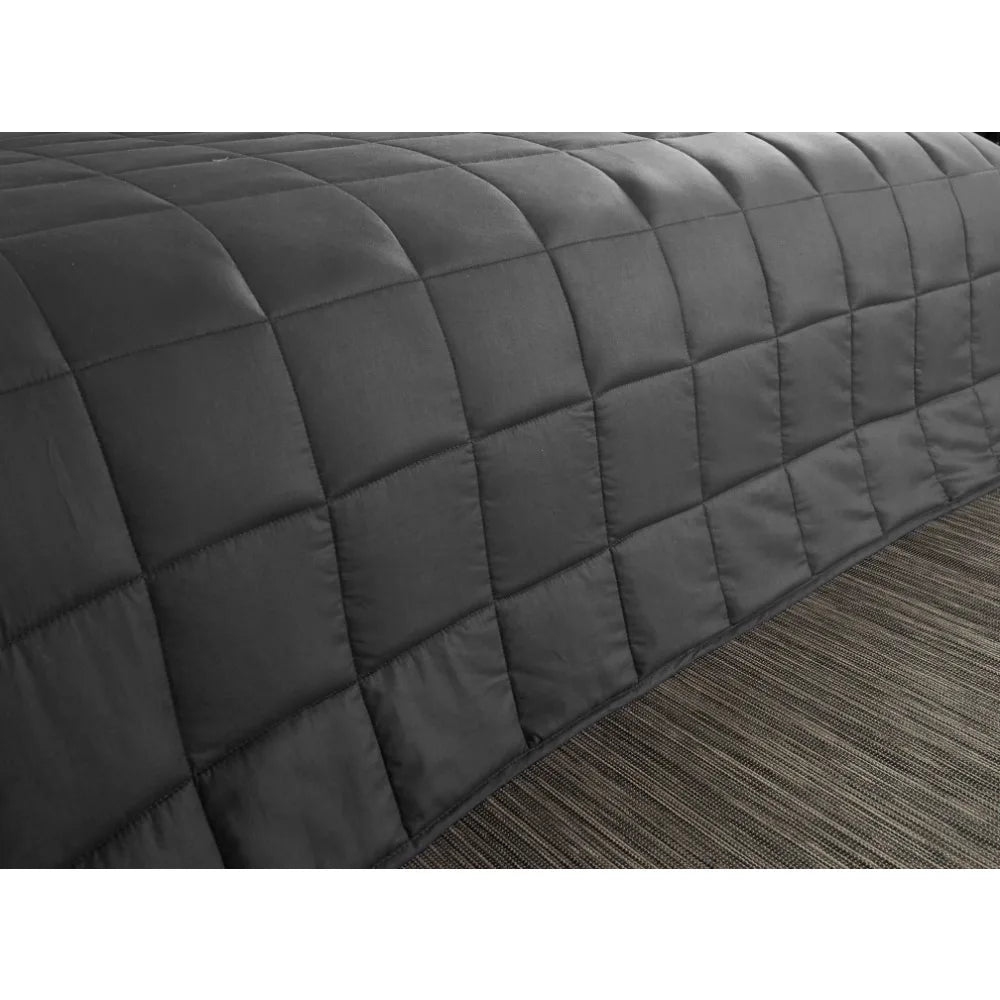 The Plush 20lb Soft Weighted Blanket, expertly crafted with a quilted dark gray grid pattern, drapes over the beds edge on a textured gray and brown striped rug, showcasing Origin USs exquisite design.
