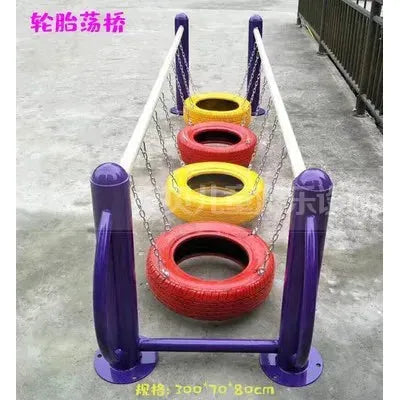 The Outdoor Steel Climbing Frame Swing serves as a vibrant playground centerpiece with suspended red, yellow, and orange tire rings on chains between two purple poles. Its paved ground encourages children to explore sensory integration through active play.