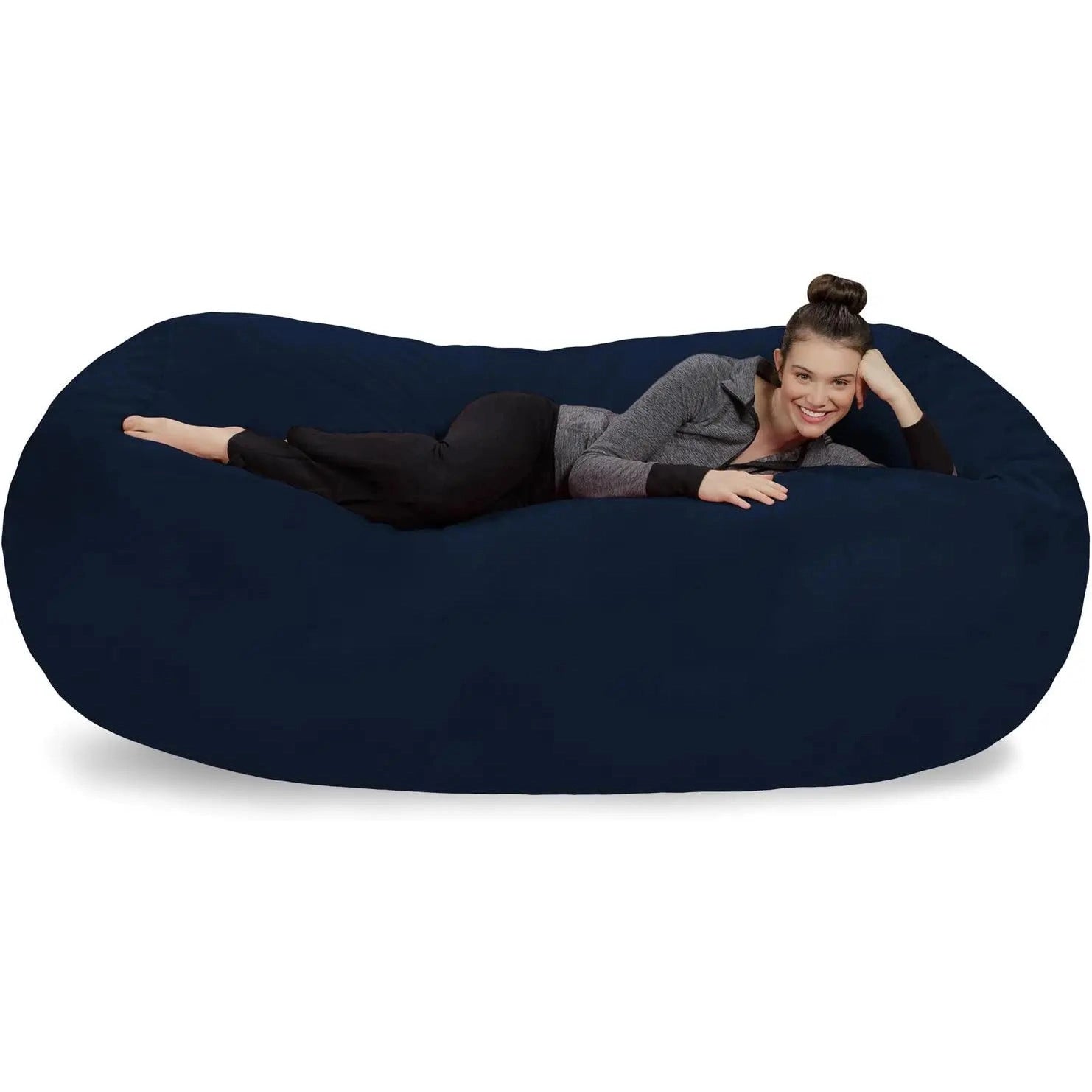 A dark-haired woman in a gray zip-up top and black pants lies on her side, smiling at the camera, atop a navy Bean Bag Lounger - Plush Sofa with Soft Microsuede Cover.